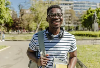 A young man carrying a backpack and smiling in an outdoor setting