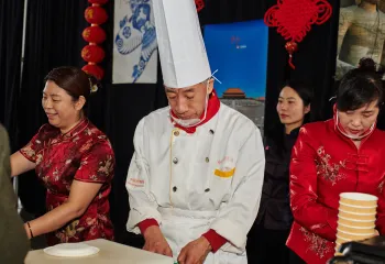 A chef and three other people preparing and serving food at the Chinese food booth.