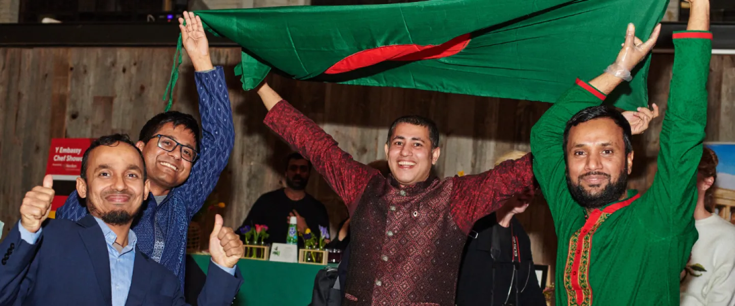 Four people holding up a large Bangladesh flag and smiling