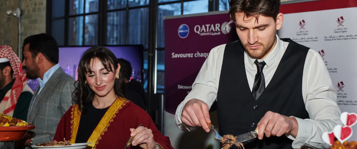 Two people serving food at the Qatar booth