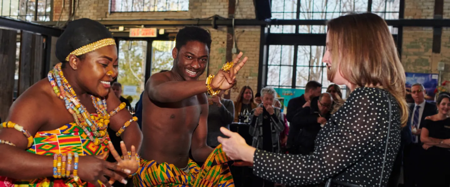 Two dancers wearing traditional Ghanaian attire and dancing with a spectator