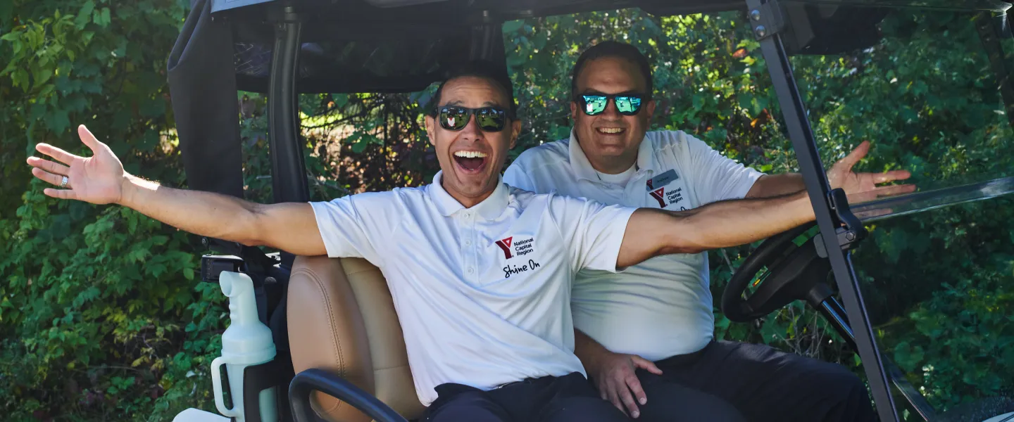 Morgan and Andrew from the YMCA sitting in a golf cart, smiling. Morgan has his arms outstretched.