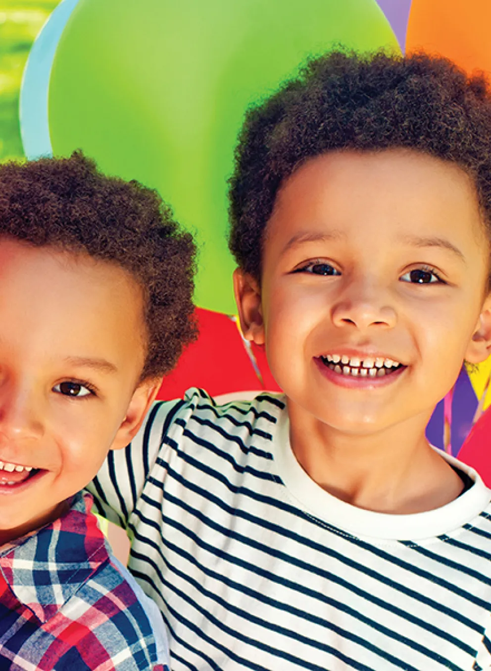 Two young boys smile joyfully in front of a vibrant display of colorful balloons.