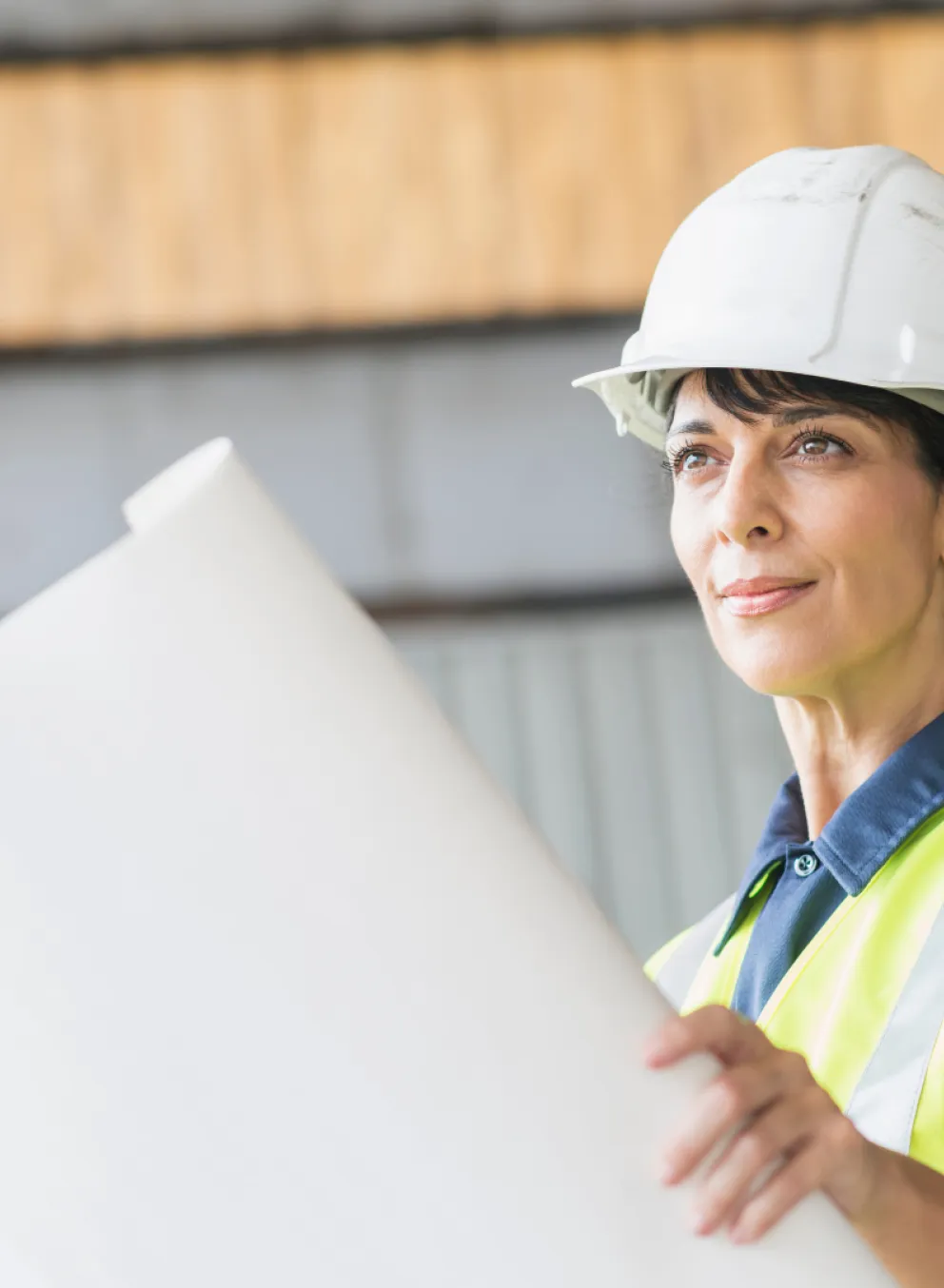 A woman in construction gear, holding a large blueprint