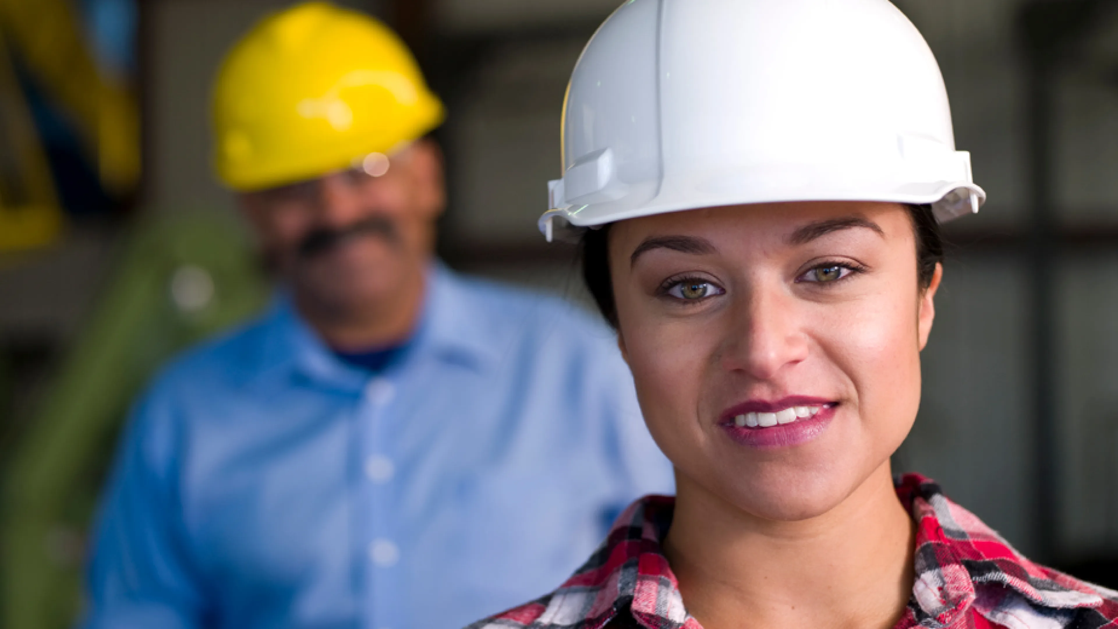 A woman wearing a white hard hat looks into the camera.