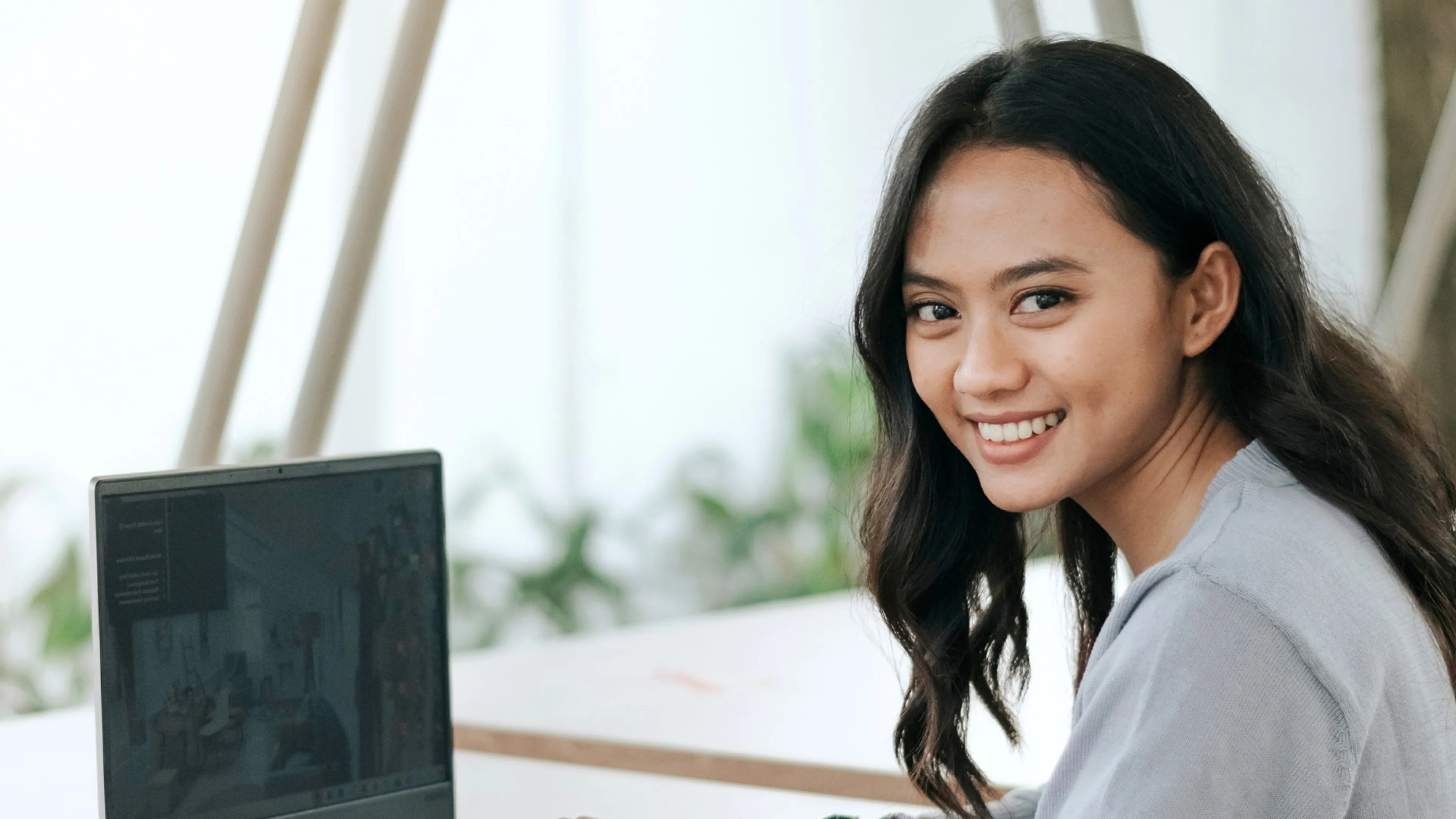 A young Asian woman smiles while working on her laptop.