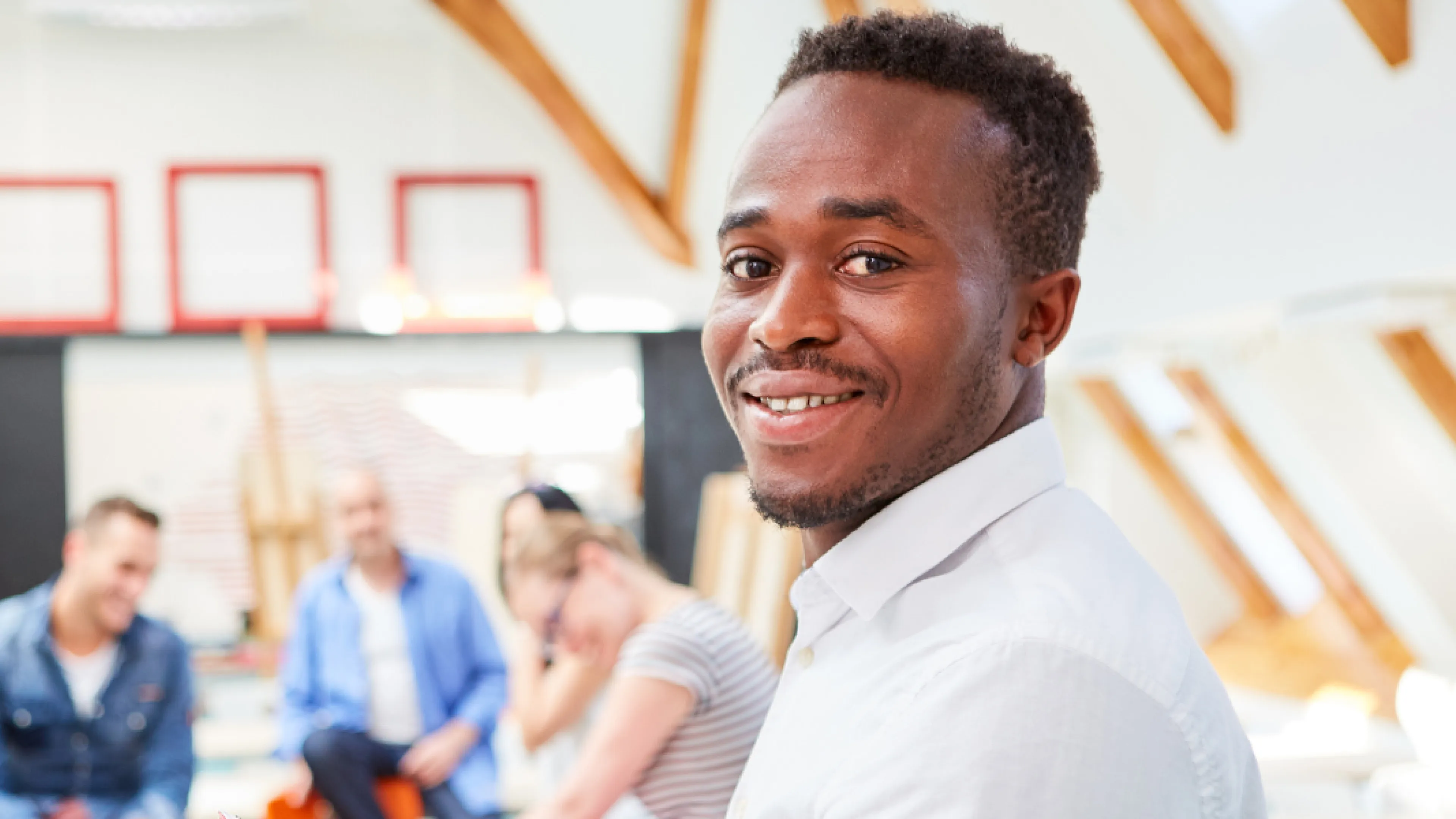 Man sits in room with other people, smiling.