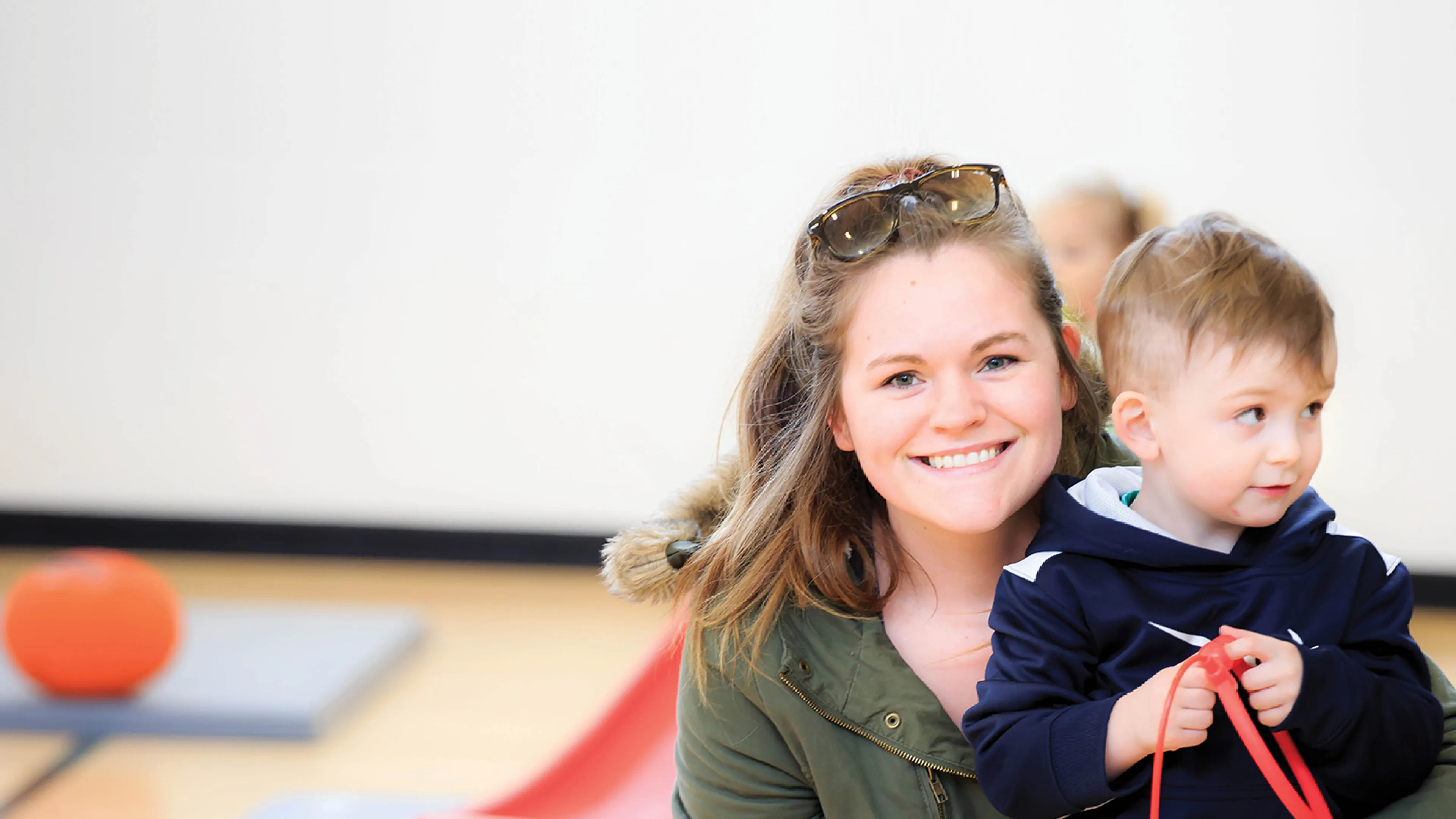 A mother and her son sit on the gymnasium floor.