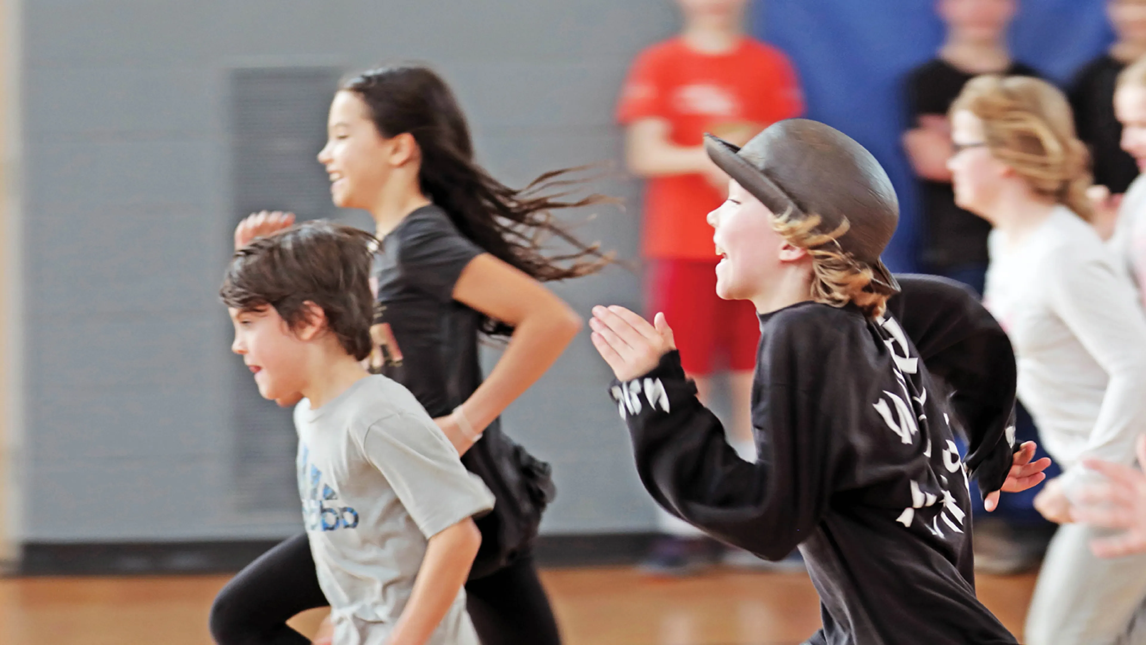 A group of children run in a gymnasium.