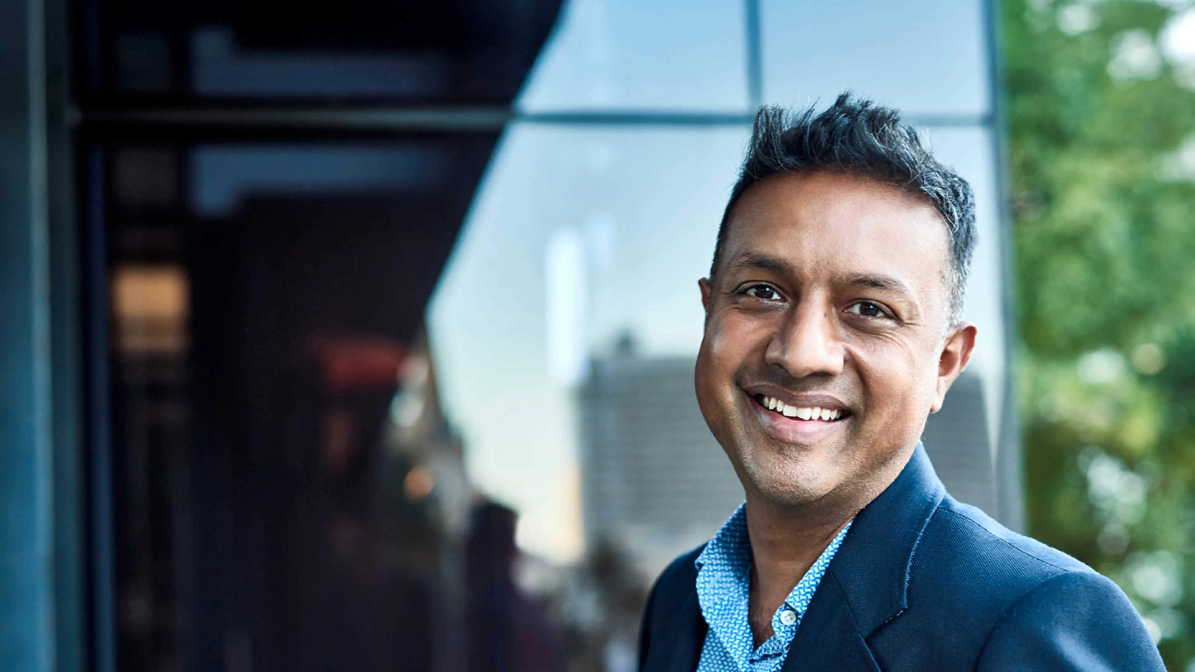 A smiling man stands outside the entrance to an office building.