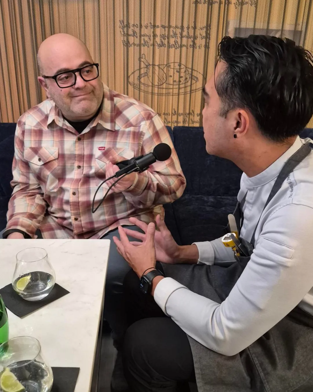 CBC's Mario Carlucci holding a microphone toward Chef David Vinoya. They are sitting on a couch.
