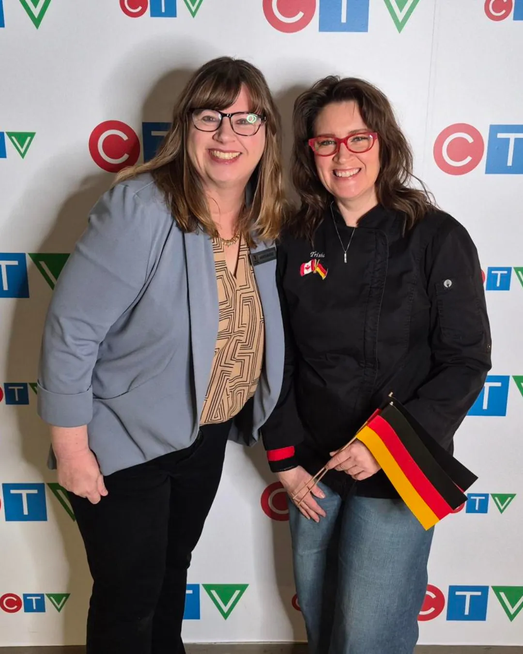 Marianne Long and Chef Trisha Donaldson in front of a CTV backdrop. Trisha is holding two small German flags.