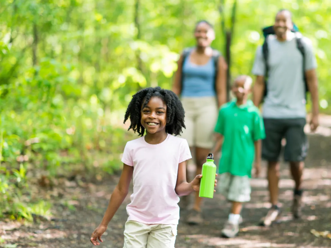 young girl walking in the woods holding a water bottle with family walking behind