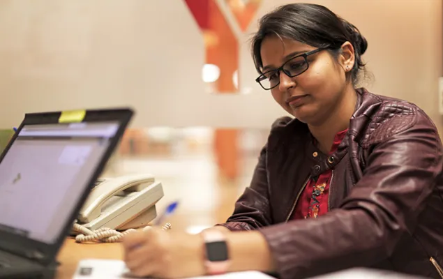 A woman wearing glasses is focused on her laptop, engaged in work at a desk.