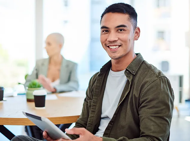 A man seated at a table, focused on using a tablet in front of him.