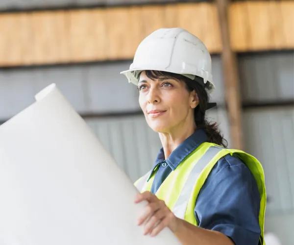 A woman in construction gear, holding a large blueprint