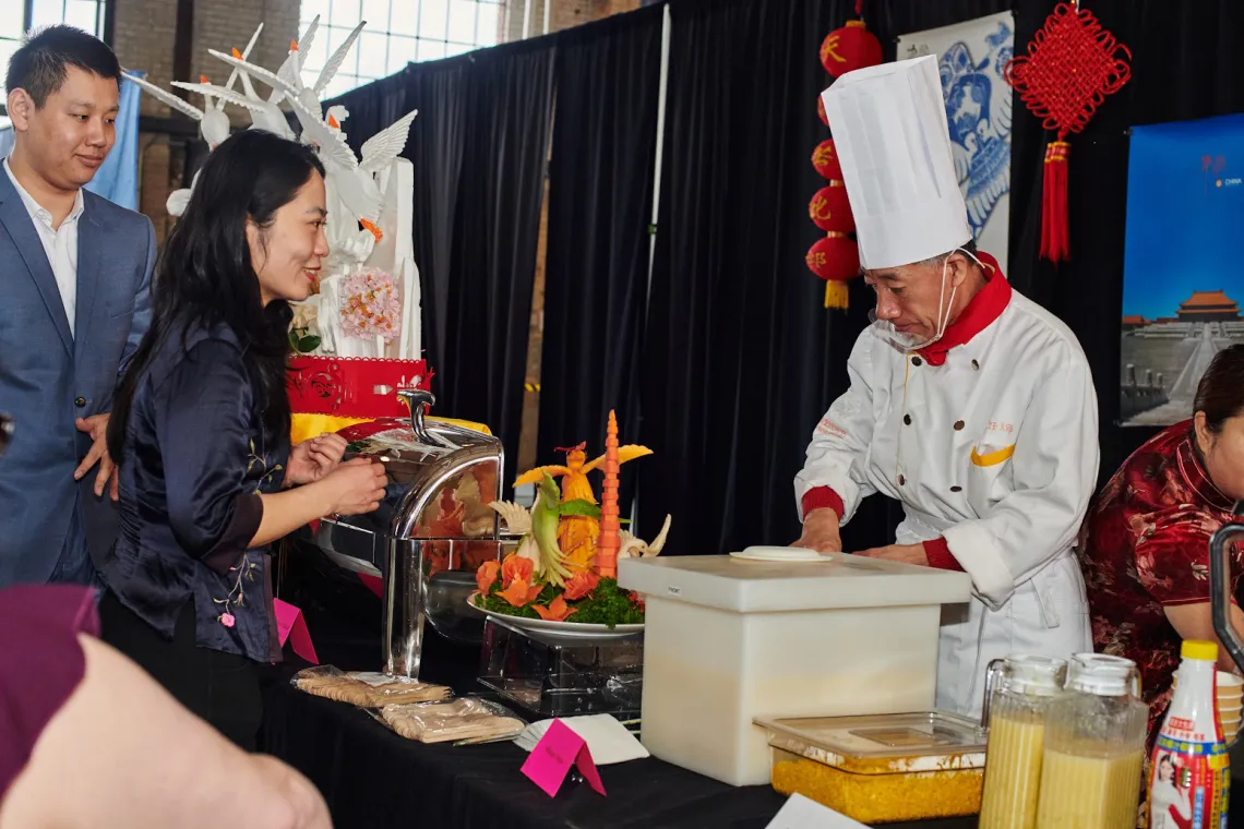 A chef wearing a hat serves delicious food to guests.