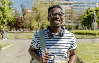 A young man carrying a backpack and smiling in an outdoor setting