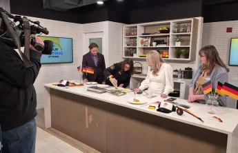 Will Aiello, Chef Trisha Donaldson, Melissa Lamb, and Marianne Long standing behind a counter on the set of CTV News Your Morning Kitchen. A camera operator is filming them.