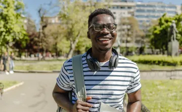 A young man carrying a backpack and smiling in an outdoor setting