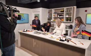 Will Aiello, Chef Trisha Donaldson, Melissa Lamb, and Marianne Long standing behind a counter on the set of CTV News Your Morning Kitchen. A camera operator is filming them.
